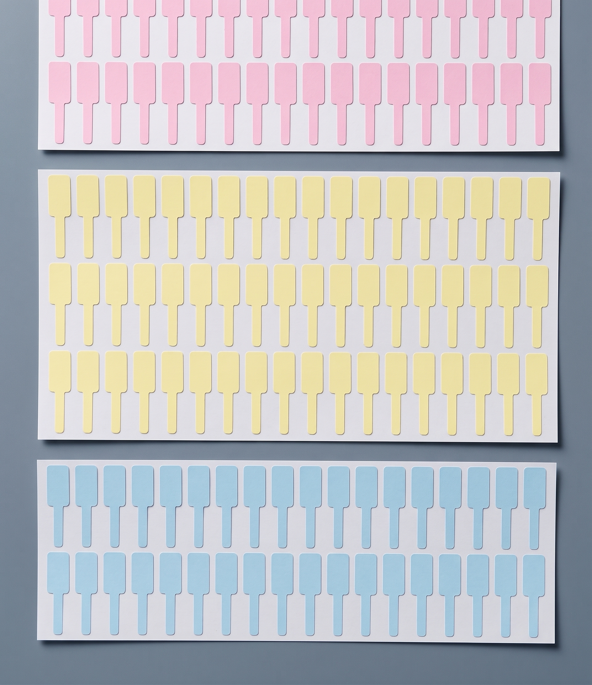 Sheets of blank dumbbell jewellery price tags in pink, yellow and blue, die-cut on release liner